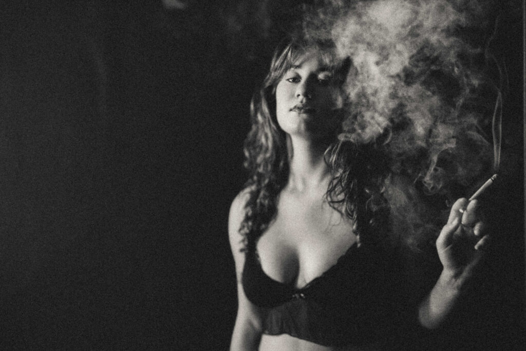 Woman in a smoky 1970s-inspired boudoir portrait with warm editorial lighting.