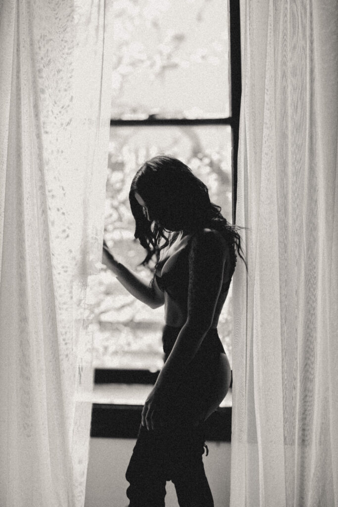 Editorial boudoir portrait of woman reflecting with soft natural window light.